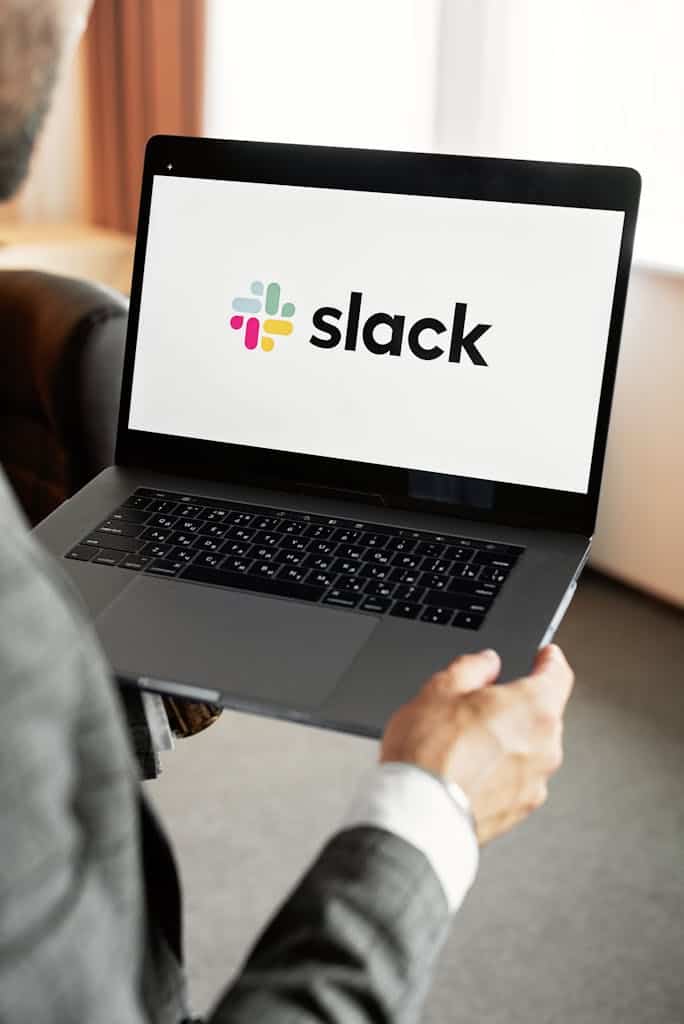 Person in Gray Long Sleeve Shirt Holding a Laptop with Slack logo